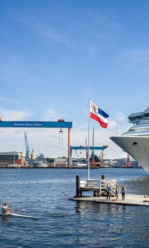 Kreuzfahrtschiff am Anleger in Kiel mit Blick auf die Werft German Naval Yards und Menschen am Steg bei sonnigem Wetter