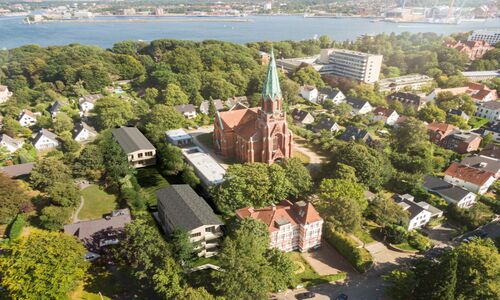 Luftaufnahme eines Wohngebiets mit einer großen roten Kirche in der Mitte, umgeben von Bäumen und mehreren Häusern